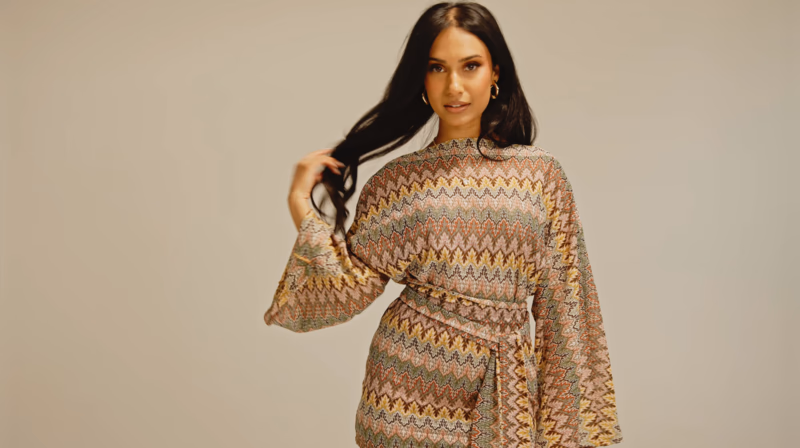 Woman in patterned knit cardigan with warm earth tones against neutral background.